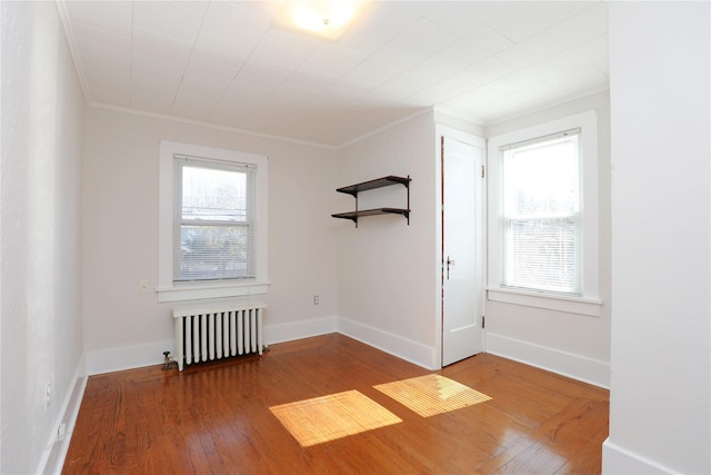 empty room with baseboards, ornamental molding, wood finished floors, and radiator