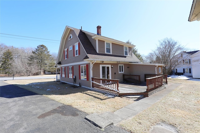 colonial inspired home with roof with shingles, a chimney, a wooden deck, and a gambrel roof