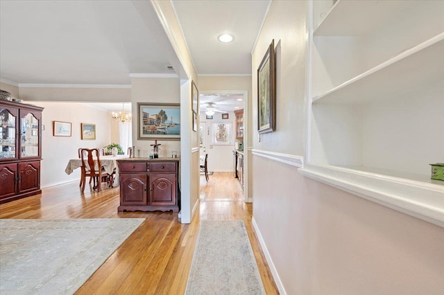 corridor featuring baseboards, an inviting chandelier, light wood-style flooring, and crown molding