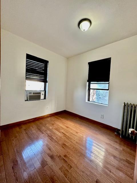 unfurnished room featuring radiator, a healthy amount of sunlight, and hardwood / wood-style floors