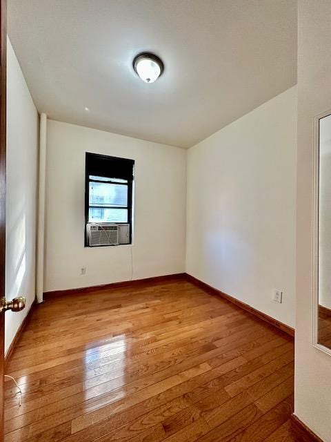 empty room featuring light wood-type flooring, cooling unit, and baseboards