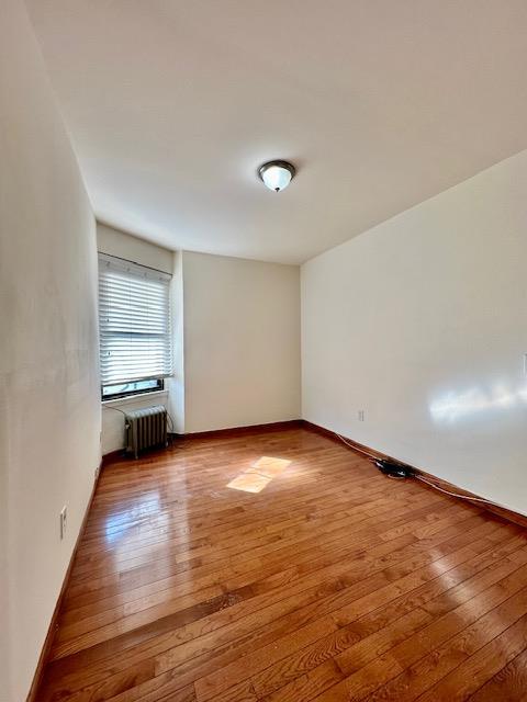 spare room featuring baseboards, hardwood / wood-style floors, and radiator