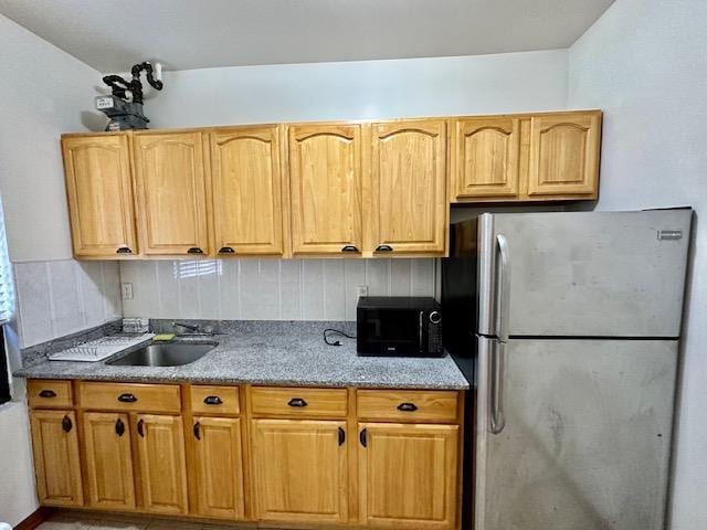 kitchen with freestanding refrigerator, black microwave, a sink, and light stone countertops