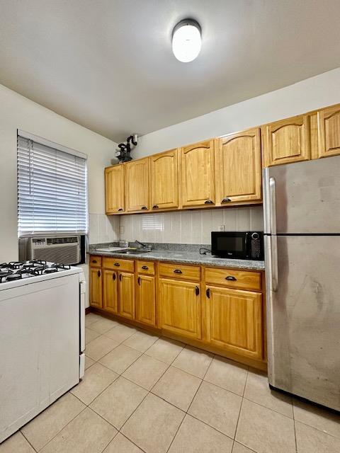 kitchen with black microwave, light tile patterned flooring, a sink, freestanding refrigerator, and gas range gas stove