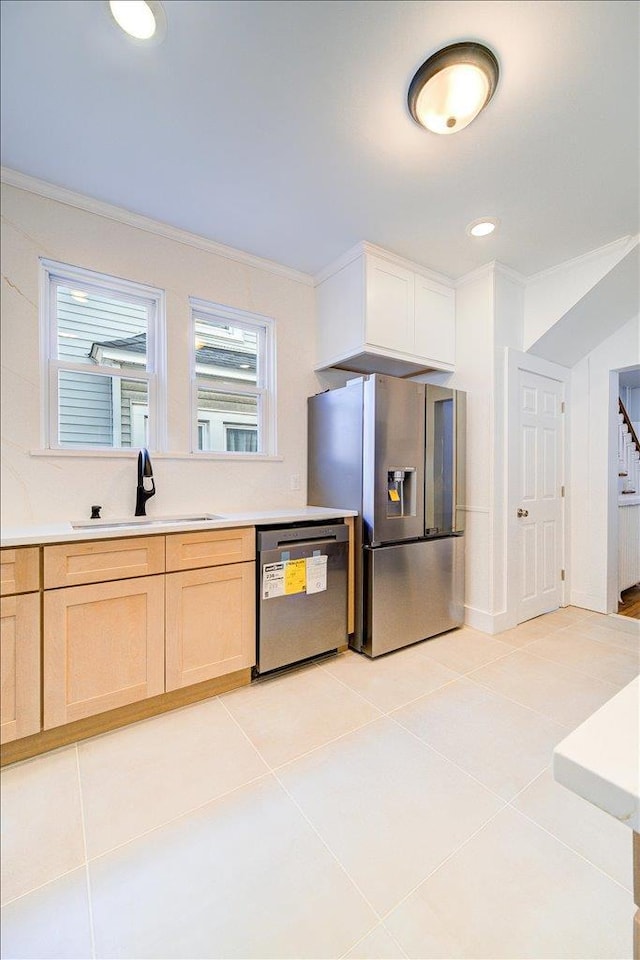 kitchen featuring light brown cabinets, crown molding, light tile patterned floors, stainless steel appliances, and a sink