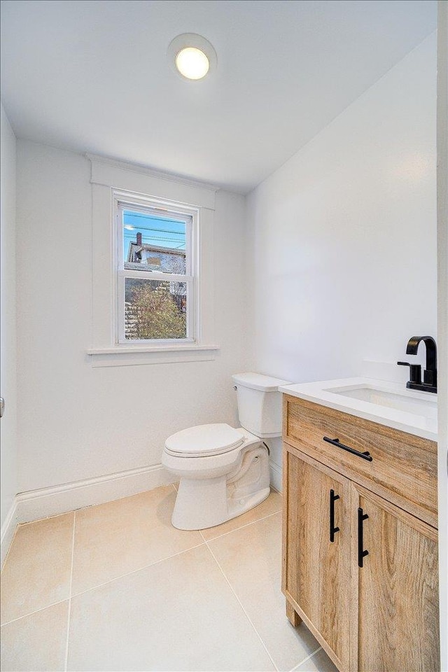 half bath featuring baseboards, toilet, vanity, and tile patterned flooring