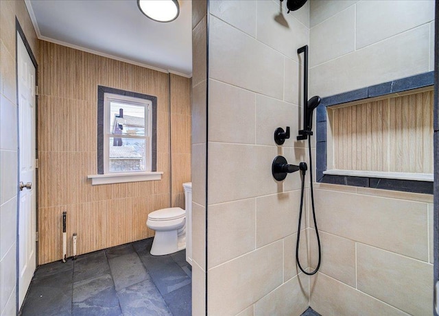 bathroom with a tile shower, stone finish floor, toilet, and tile walls