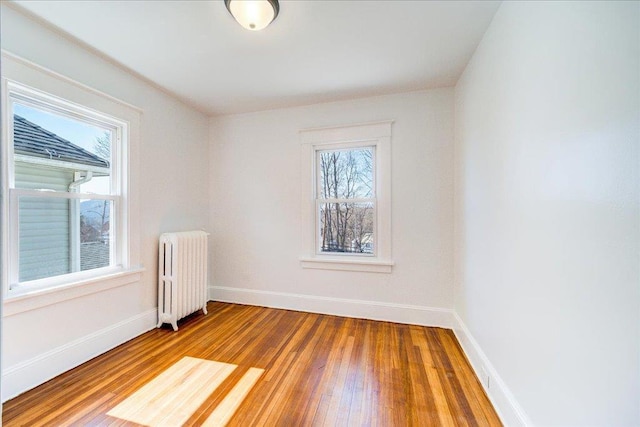 spare room featuring hardwood / wood-style floors, radiator heating unit, and baseboards