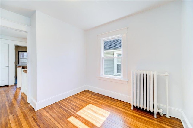 empty room featuring radiator heating unit, baseboards, and wood-type flooring