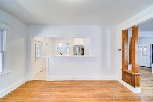 unfurnished living room with light wood finished floors, baseboards, and ornate columns