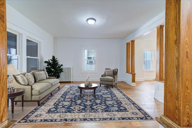 living room featuring ornate columns, radiator, baseboards, and wood finished floors