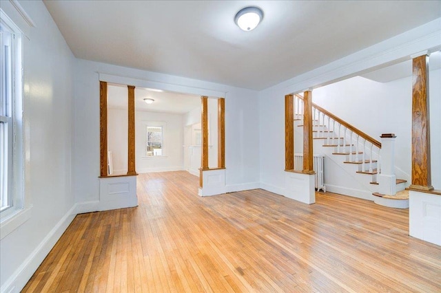 empty room featuring stairs, radiator, baseboards, and light wood finished floors