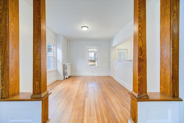 unfurnished living room with light wood-style flooring, radiator heating unit, baseboards, and ornate columns