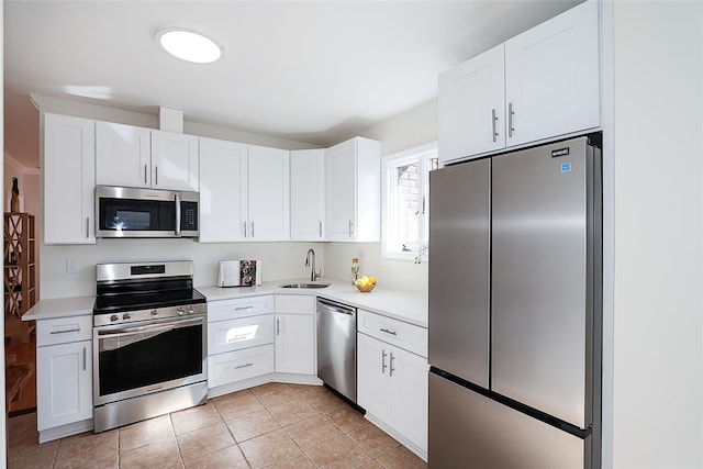 kitchen with light tile patterned floors, stainless steel appliances, light countertops, white cabinetry, and a sink