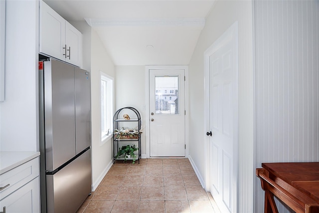 doorway to outside with vaulted ceiling, light tile patterned flooring, and baseboards