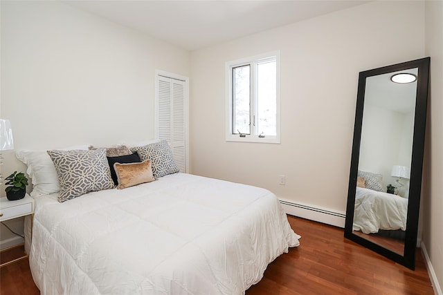 bedroom with a closet, baseboard heating, and wood finished floors