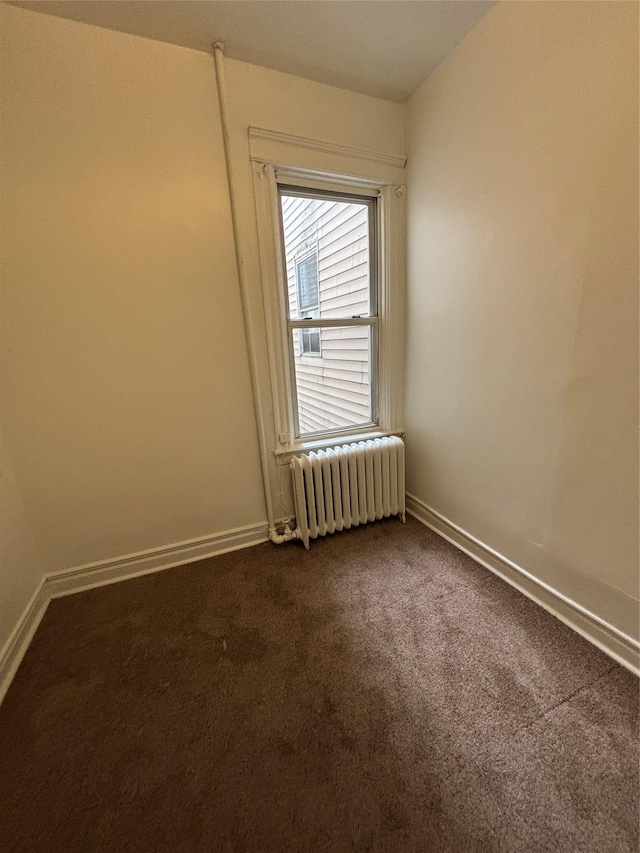 empty room with dark colored carpet, baseboards, and radiator