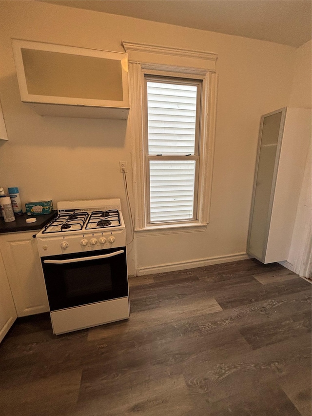 kitchen with baseboards, dark wood-style flooring, white gas range oven, white cabinetry, and dark countertops