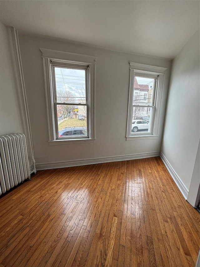 unfurnished room with radiator heating unit, baseboards, wood-type flooring, and a wealth of natural light