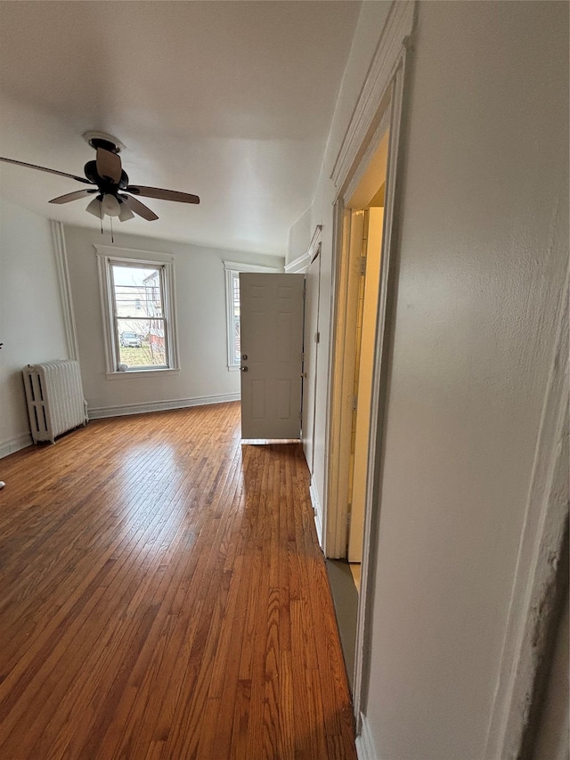 unfurnished room with radiator heating unit, baseboards, wood-type flooring, and ceiling fan