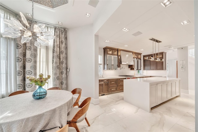 kitchen featuring light countertops, wall chimney range hood, glass insert cabinets, and marble finish floor