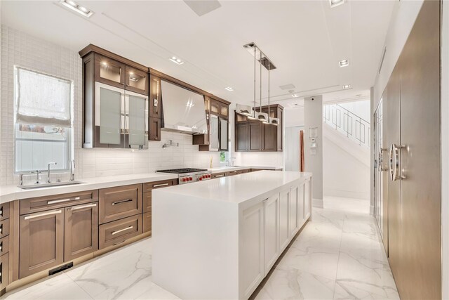 kitchen featuring marble finish floor, glass insert cabinets, wall chimney range hood, and a sink