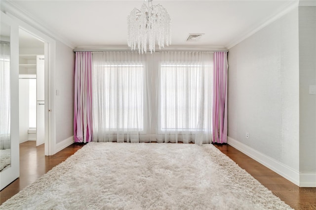 empty room with crown molding, a notable chandelier, wood finished floors, and visible vents