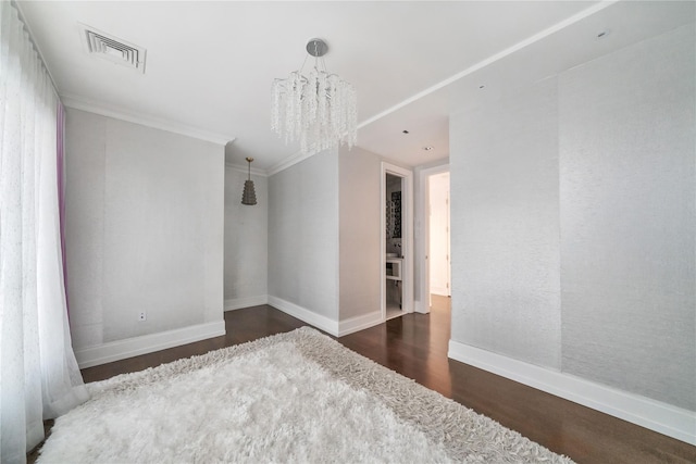 spare room with visible vents, ornamental molding, wood finished floors, baseboards, and a chandelier