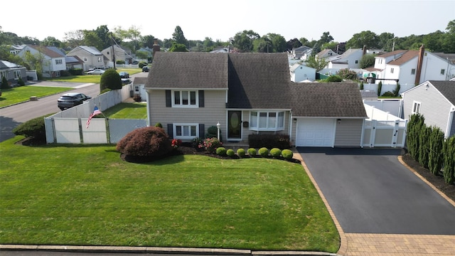 view of front facade featuring a front lawn, aphalt driveway, a residential view, an attached garage, and a gate