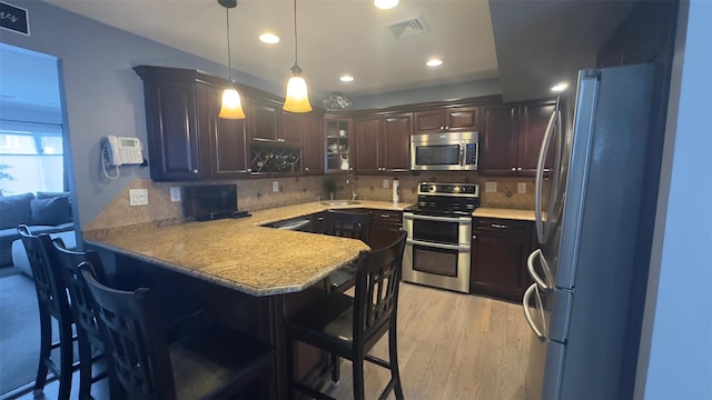 kitchen featuring visible vents, dark brown cabinetry, a peninsula, stainless steel appliances, and a sink