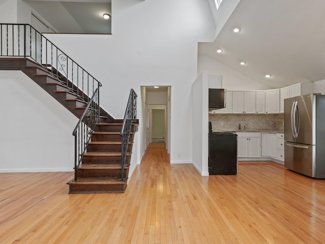 kitchen with black gas stove, light countertops, freestanding refrigerator, white cabinets, and high vaulted ceiling