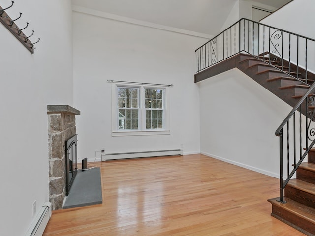 living area featuring baseboard heating, stairway, a stone fireplace, and wood finished floors