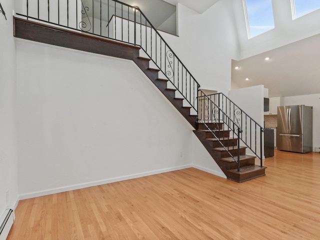 staircase featuring wood finished floors, baseboards, a skylight, a towering ceiling, and a baseboard heating unit