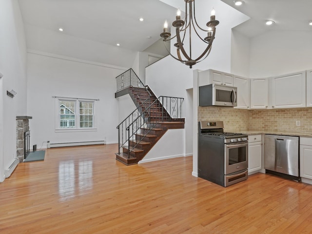 kitchen with a baseboard heating unit, appliances with stainless steel finishes, a fireplace, white cabinets, and high vaulted ceiling