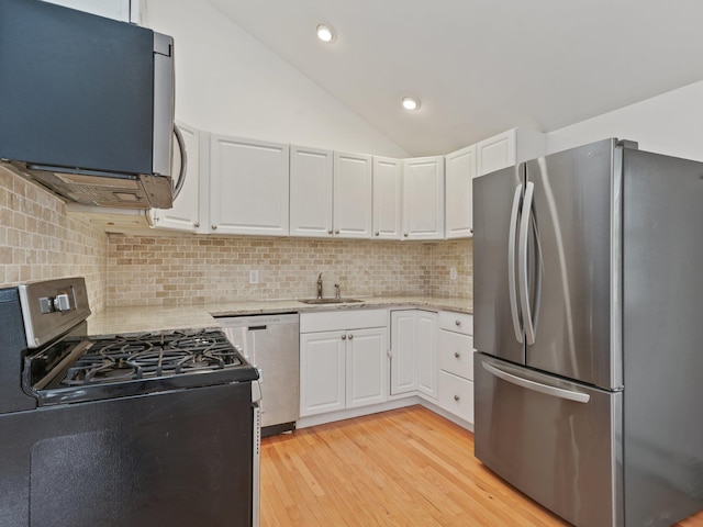 kitchen with a sink, stainless steel appliances, white cabinets, lofted ceiling, and light stone countertops