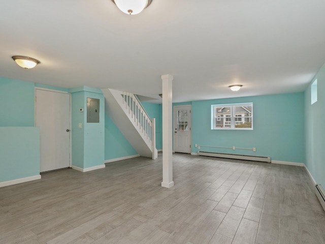 basement featuring a baseboard heating unit, light wood-style flooring, stairs, and baseboards