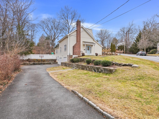 view of property exterior featuring an attached garage, fence, a lawn, a chimney, and driveway