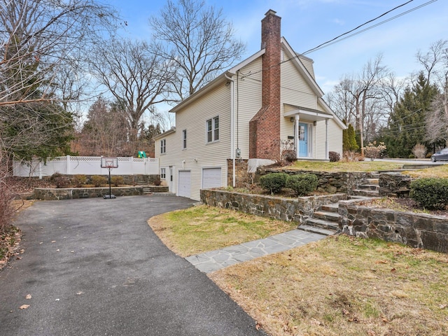 view of side of home with driveway, fence, a yard, an attached garage, and a chimney