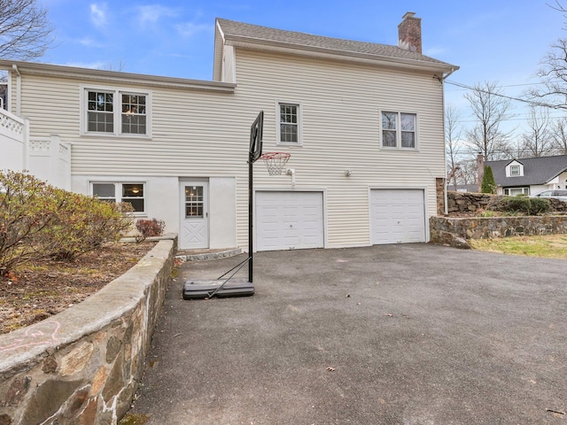 back of house featuring aphalt driveway, a chimney, and a garage