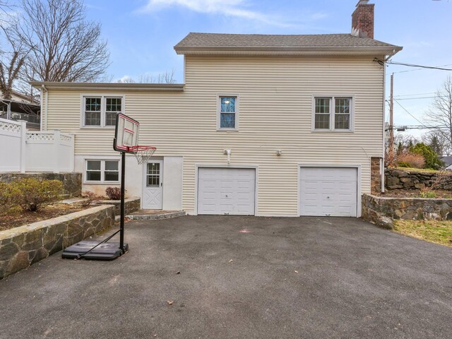 rear view of house with an attached garage, fence, driveway, and a chimney