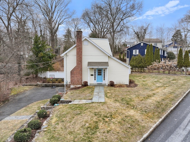 bungalow-style home with a front yard, fence, driveway, and a chimney