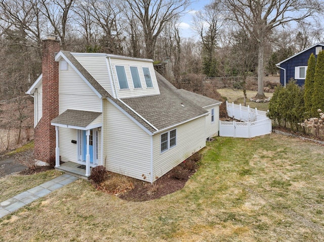 view of home's exterior with a shingled roof, a lawn, a chimney, and fence