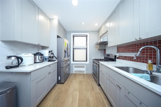 kitchen featuring light wood-style flooring, a sink, under cabinet range hood, appliances with stainless steel finishes, and light countertops