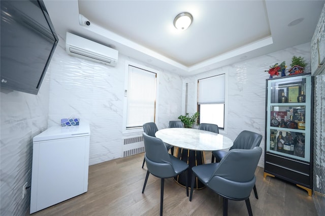 dining space with a raised ceiling, radiator heating unit, a wall unit AC, and wood finished floors