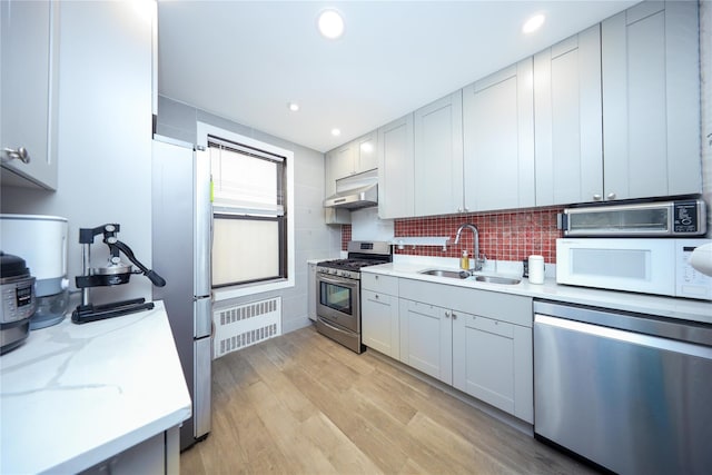 kitchen featuring light wood-type flooring, a sink, under cabinet range hood, stainless steel appliances, and decorative backsplash