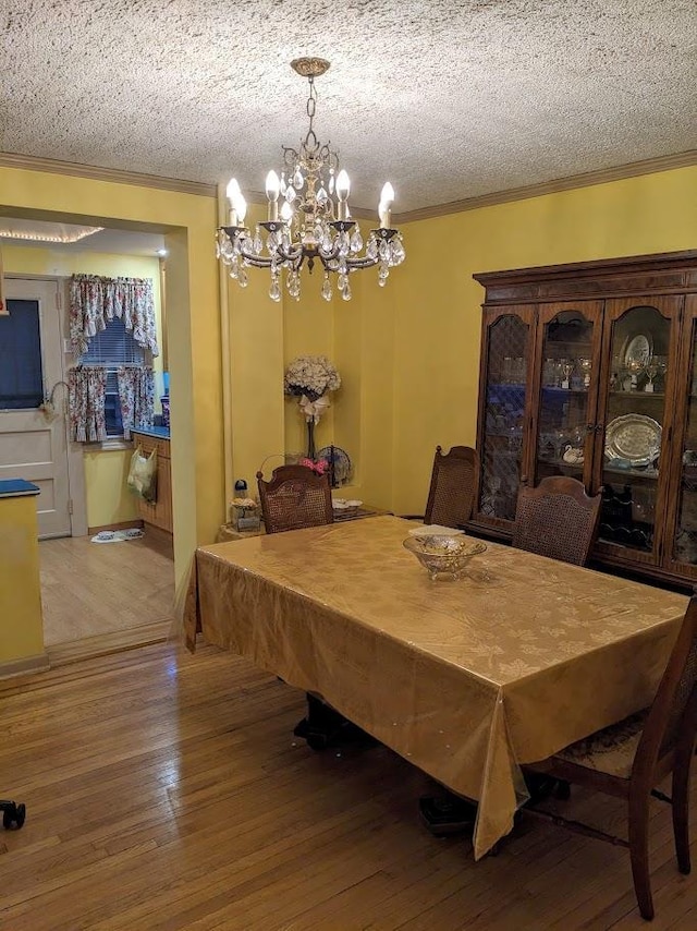 dining area with a textured ceiling, wood-type flooring, an inviting chandelier, and crown molding