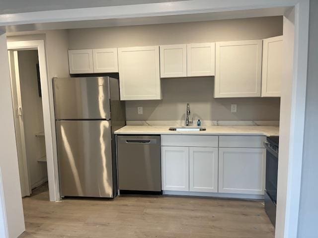 kitchen with appliances with stainless steel finishes, light wood-style floors, white cabinets, and a sink