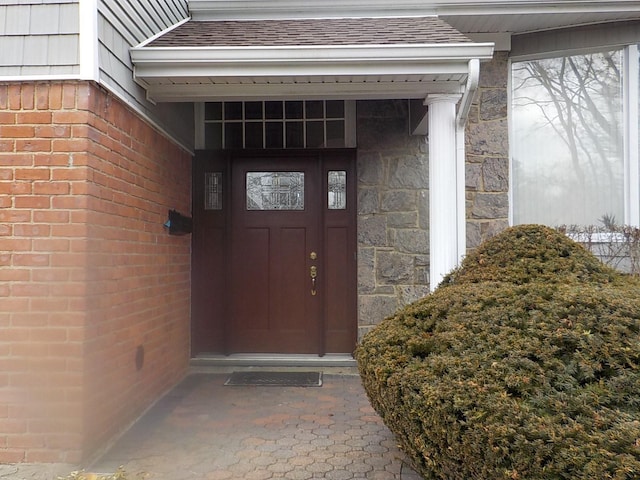 doorway to property featuring stone siding, brick siding, and a shingled roof