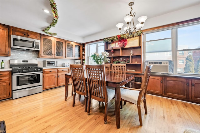 dining room with a toaster, cooling unit, light wood-style floors, and a chandelier