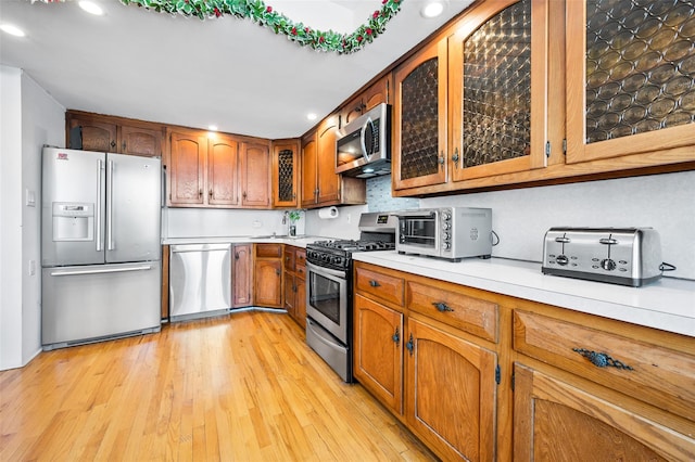 kitchen featuring a toaster, light countertops, light wood-style floors, appliances with stainless steel finishes, and brown cabinets